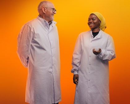 Deux employés prennent la pose devant un fond orange et se sourient mutuellement