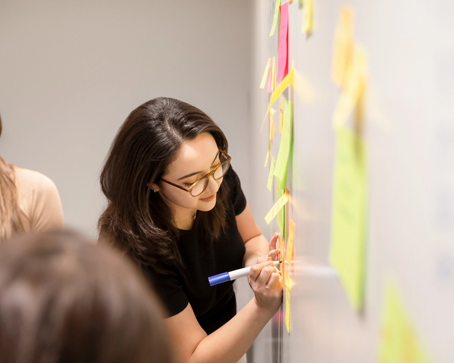 Employée qui travaille et qui écrit sur des posts it sur un tableau blanc