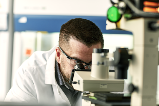 Scientifique regardant à travers un microscope dans un laboratoire