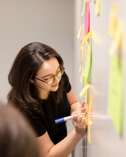 Employée qui travaille et qui écrit sur des posts it sur un tableau blanc